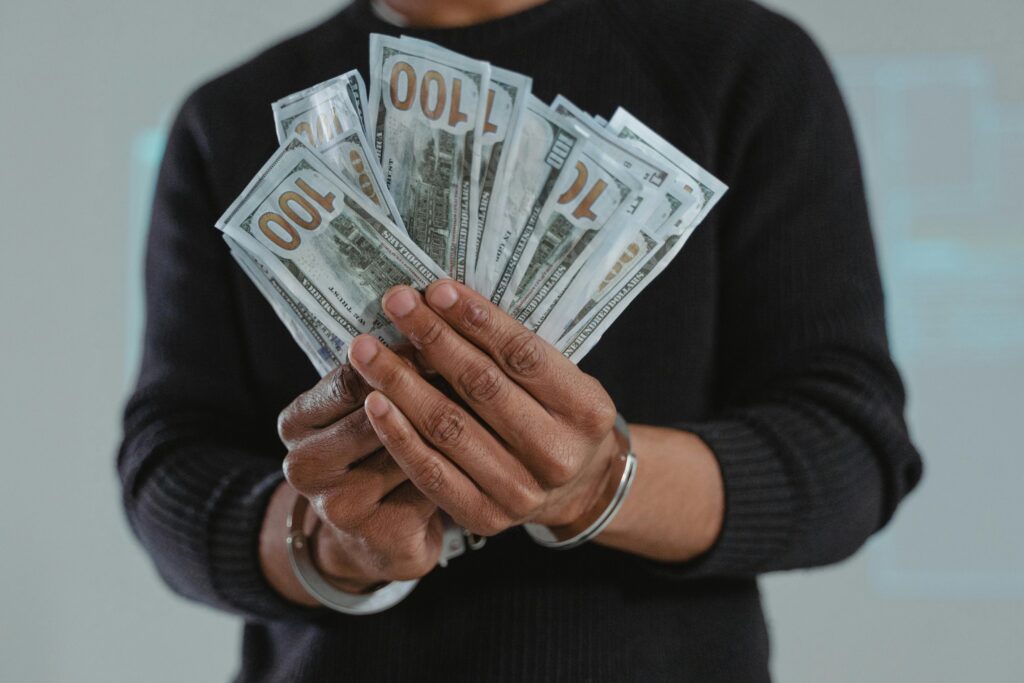 Close-up of hands holding 100-dollar bills while handcuffed, symbolizing crime and punishment.